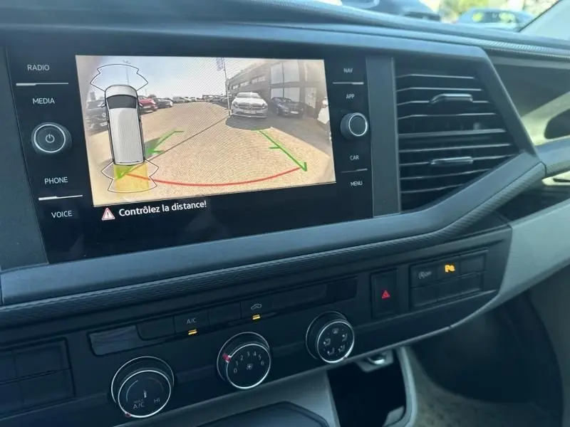 Vue intérieure du tableau de bord du Volkswagen Transporter blanc 2022, avec écran de caméra de recul et commandes climatisation visibles.