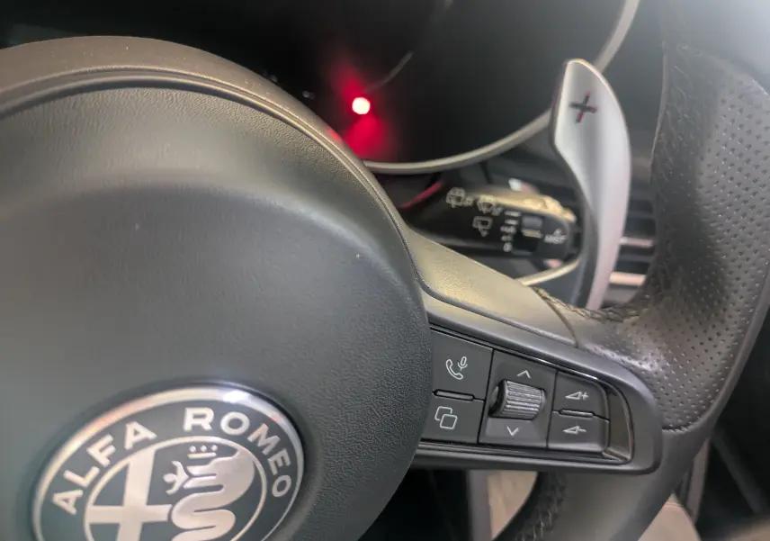 Gros plan sur le volant en cuir perforé de l'Alfa Romeo Stelvio blanc 2023 avec commandes intégrées et palettes de changement de vitesse.