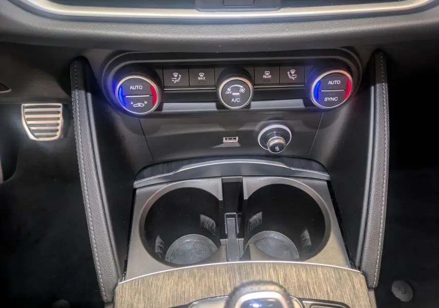 Gros plan sur la console centrale de l'Alfa Romeo Stelvio 2023, avec commandes de climatisation et porte-gobelets noirs.