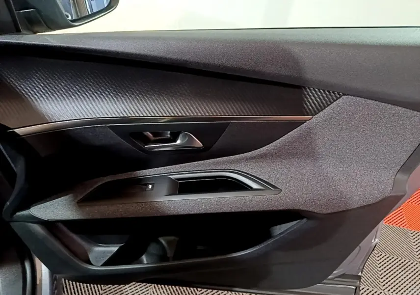Vue intérieure du panneau de porte côté conducteur de la Peugeot 3008 gris clair, avec finition tissu et insert imitation carbone.