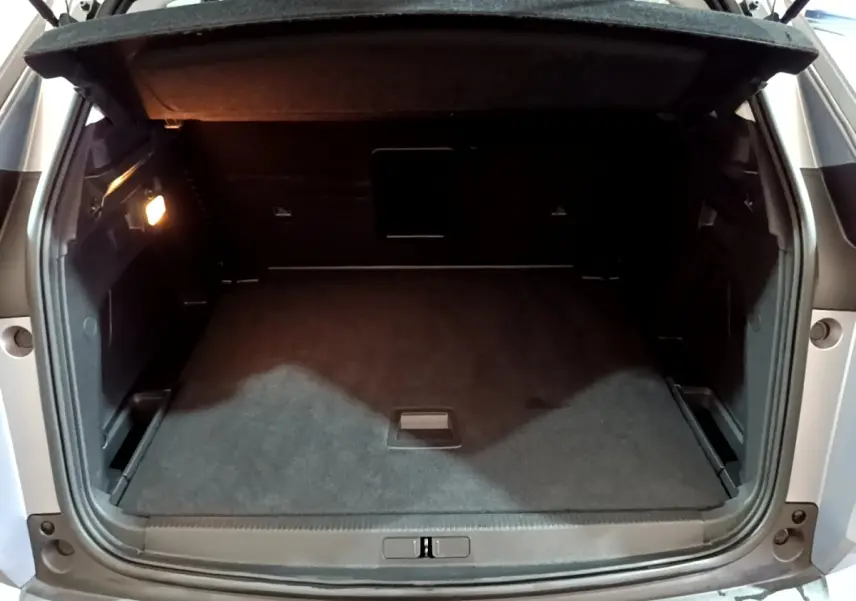 Coffre ouvert vu de l'arrière d'un Peugeot 3008 gris clair, espace de chargement propre et éclairé à gauche.
