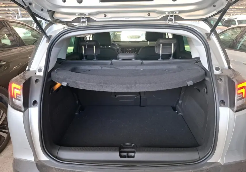 Coffre ouvert d’un Opel Crossland gris clair 2024, vue arrière montrant l’espace de chargement et la tablette cache-bagages.