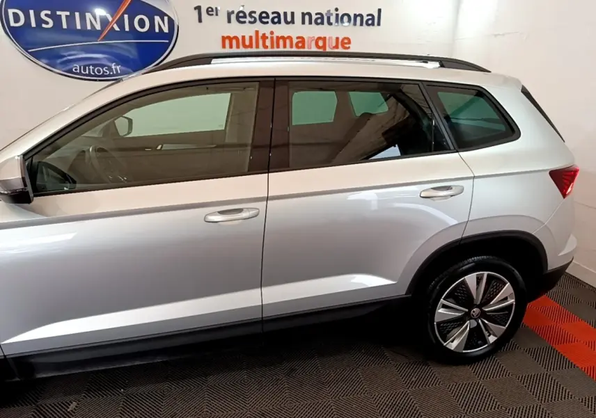 Profil droit du ŠKODA KAROQ gris clair 2022 avec jantes alliage et vitres teintées en intérieur showroom.