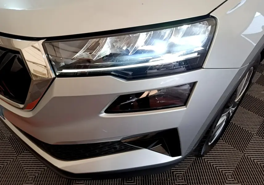 Gros plan sur l'avant droit gris clair du Skoda Karoq 2022 avec phares LED allumés et calandre chromée.