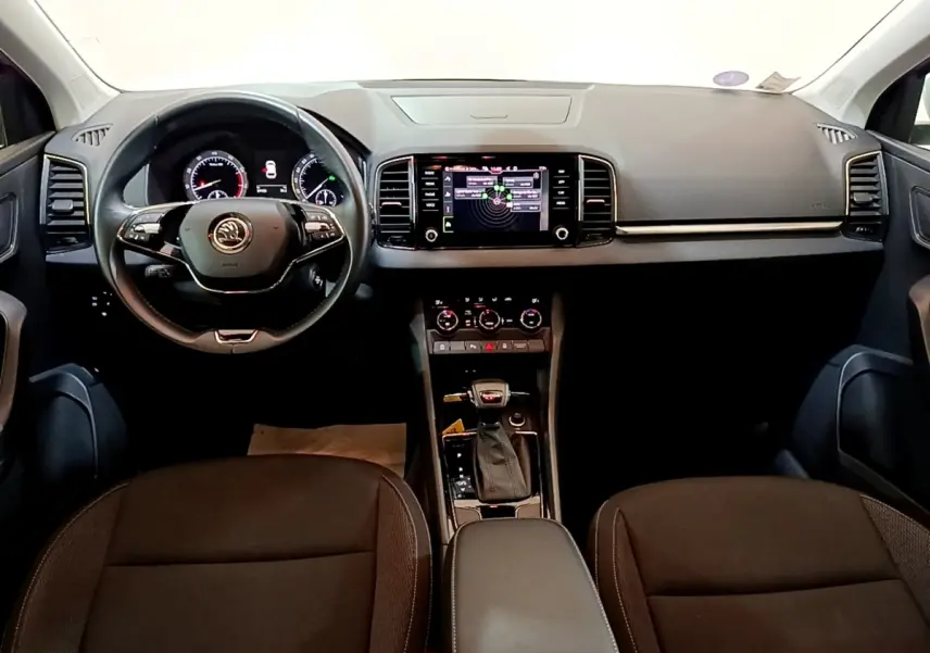Vue intérieure frontale du tableau de bord et volant cuir noir du Skoda Karoq 1.5 TSI avec écran tactile central allumé.