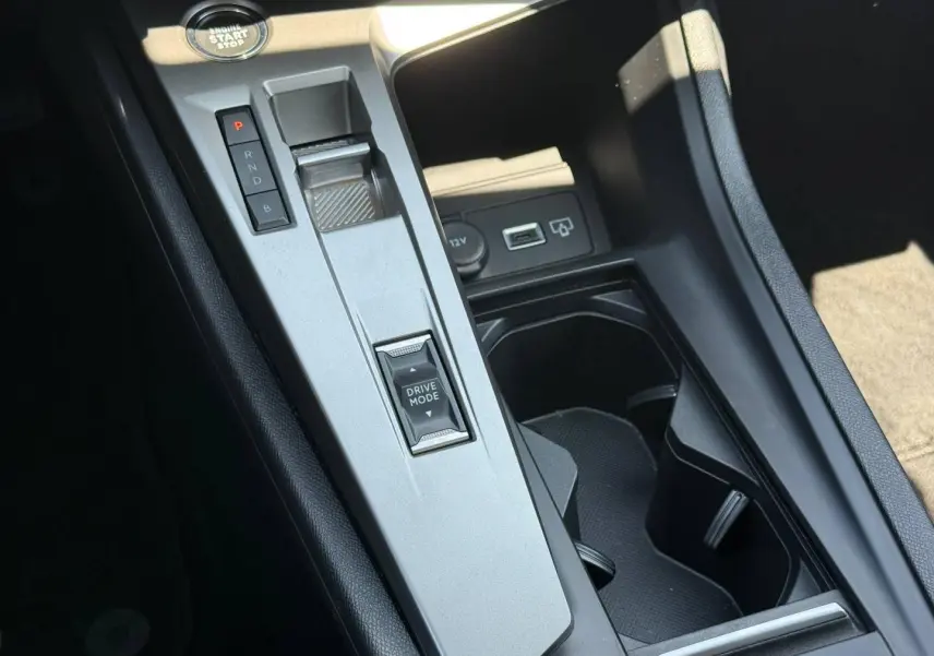 Vue rapprochée de la console centrale grise avec sélecteur de mode de conduite et bouton start/stop dans une Peugeot 308 e-308 noire.