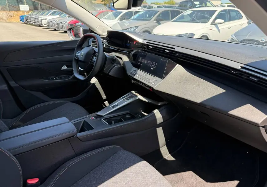 Intérieur de la Peugeot e-308 2025 vu côté conducteur, tableau de bord moderne avec écran tactile et sièges tissu gris.