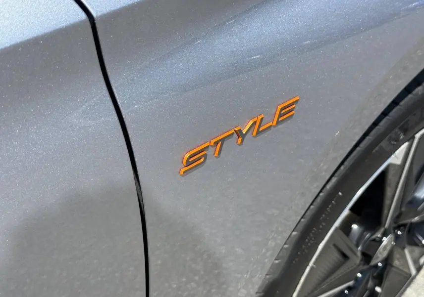 Gros plan sur l’inscription orange Style sur l’aile avant droite d’une Peugeot 308 e-308 noire avec jante alu visible.