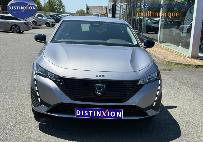 Vue avant d'une Peugeot 308 e-308 2025 gris métallisé avec calandre noire et feux LED verticaux allumés.