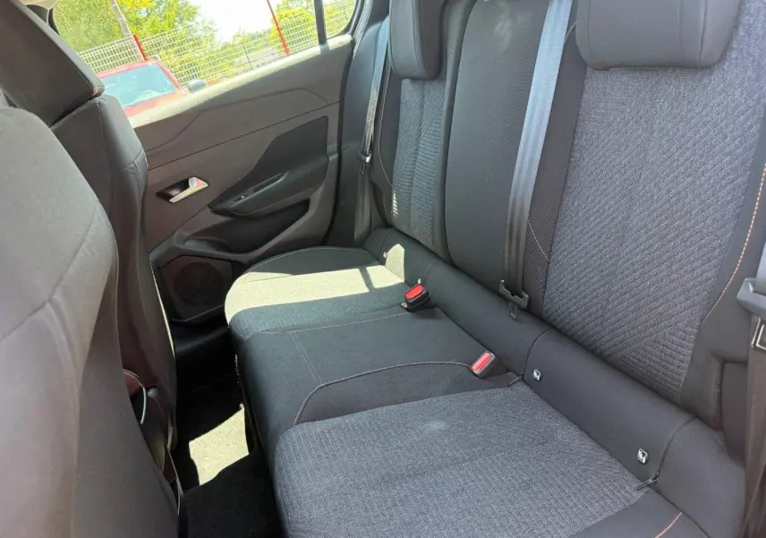 Vue intérieure côté arrière gauche montrant la banquette tissu noir et gris avec surpiqûres orange de la Peugeot e-308 2025.