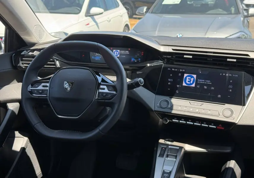 Vue intérieure du poste de conduite de la Peugeot e-308 2025, avec volant multifonction et écran tactile central.