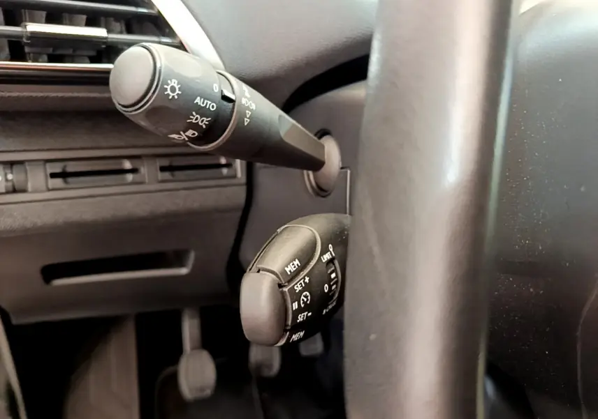 Gros plan sur les commandes au volant côté gauche du Peugeot 3008 gris foncé, avec réglages des phares et régulateur de vitesse.