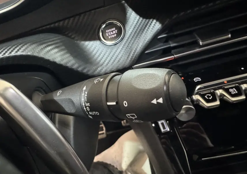 Gros plan sur la commande d’essuie-glace et bouton start/stop dans l’habitacle noir du Peugeot 208 Hybrid 136 eDCS6 GT.
