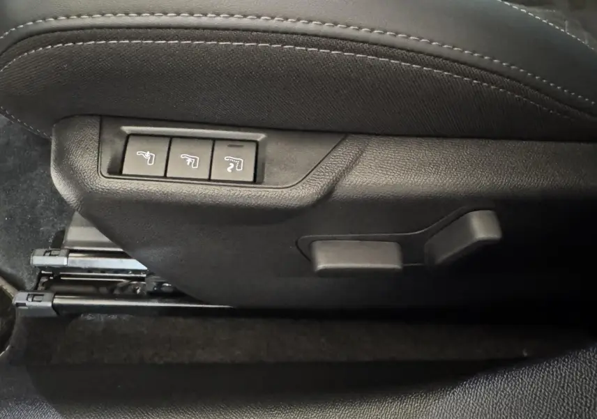 Détail des commandes de réglage électrique du siège avant côté conducteur, tissu noir avec surpiqûres grises.