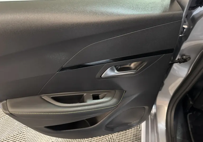 Vue intérieure de la porte arrière droite gris clair de la Peugeot 208 Hybrid 136 eDCS6 GT avec poignée argentée et surpiqûres vertes.