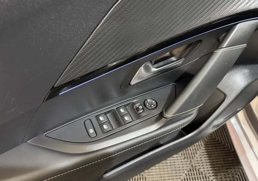 Détail de la porte côté conducteur de la Peugeot 208 Hybrid gris clair, avec commandes électriques et surpiqûres vertes.