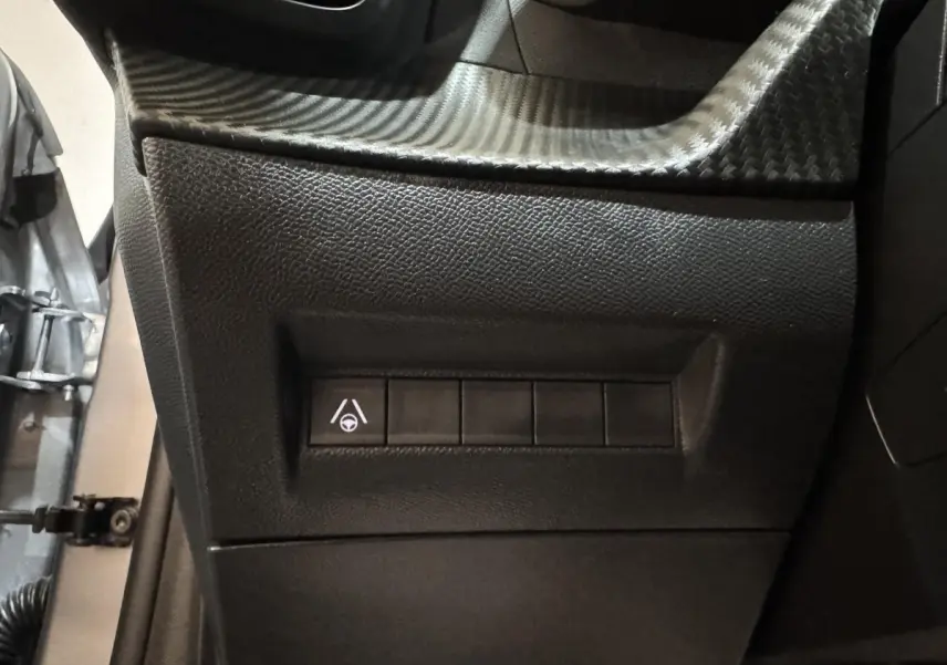 Gros plan sur les commandes latérales noires du tableau de bord d'une Peugeot 208 Hybrid gris clair, côté conducteur.