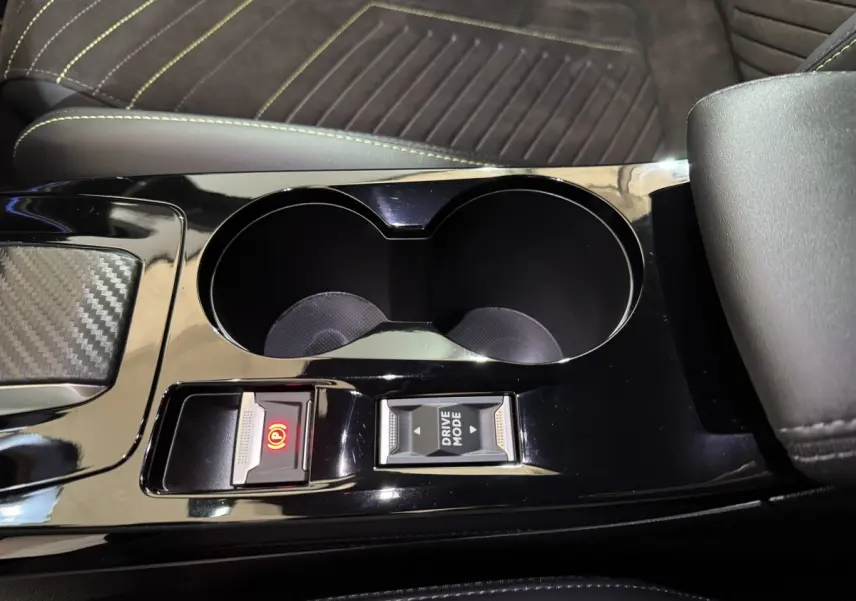 Gros plan sur la console centrale noire brillante de la Peugeot 208 Hybrid 136 eDCS6 GT avec porte-gobelets et commandes électriques.