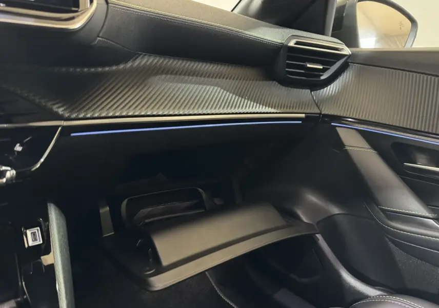 Intérieur côté passager de la Peugeot 208 Hybrid gris clair, tableau de bord avec finition carbone et éclairage d'ambiance bleu.