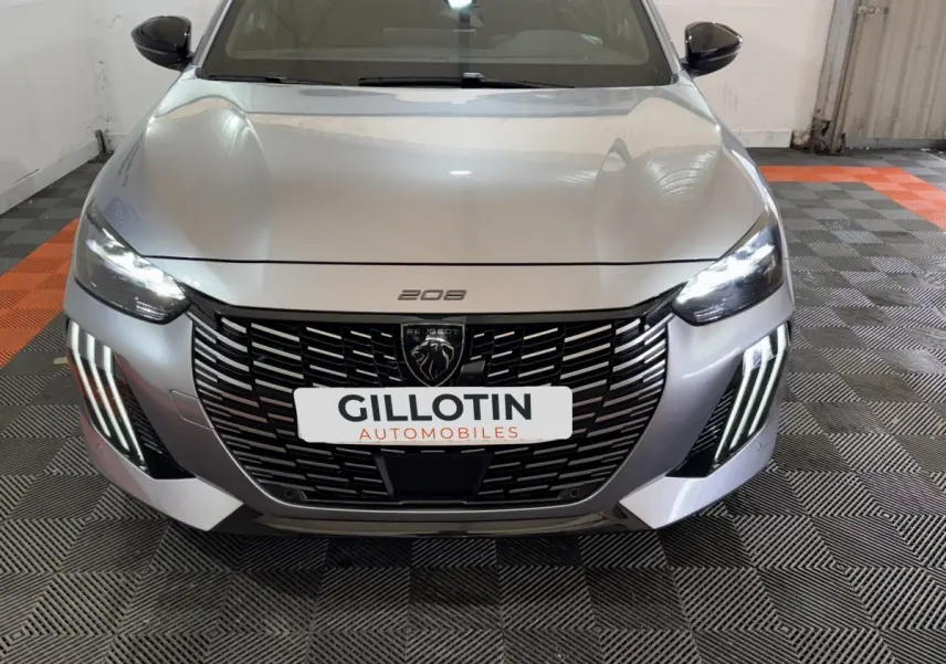 Vue avant frontale d'une Peugeot 208 Hybrid 136 eDCS6 GT gris clair avec calandre noire et feux LED allumés.