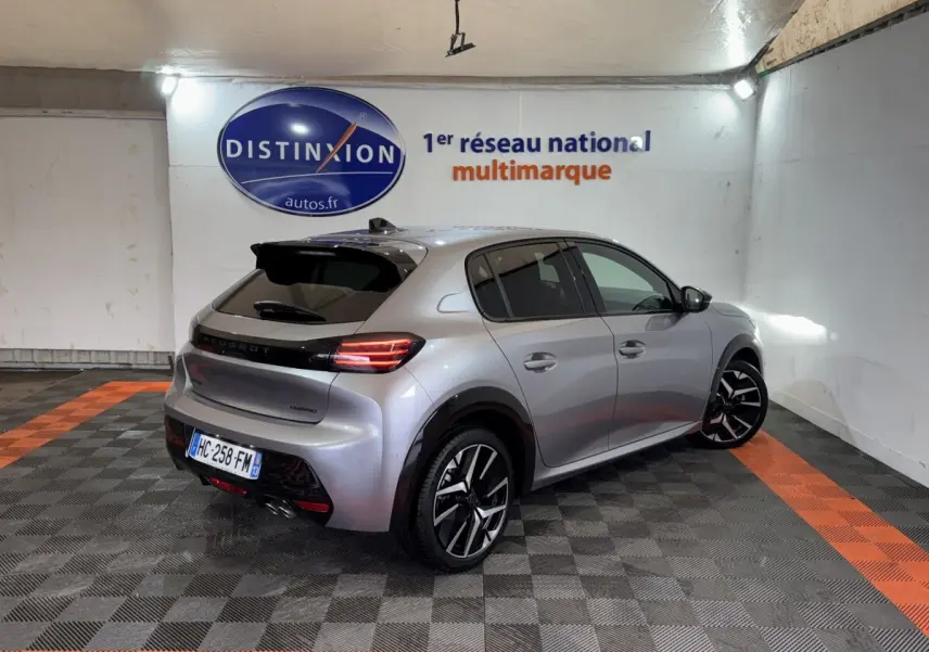 Peugeot 208 Hybrid gris clair vue 3/4 arrière droit dans un showroom avec sol à damiers noir et orange.