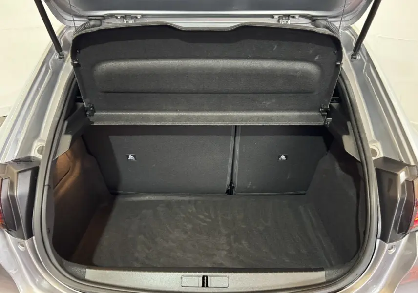 Coffre ouvert vu de l'arrière d'une Peugeot 208 Hybrid 136 eDCS6 GT gris clair, espace de chargement vide et propre.