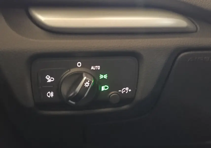 Gros plan sur le bouton de commande des phares avec éclairage vert, tableau de bord noir de l'Audi A3 blanc.