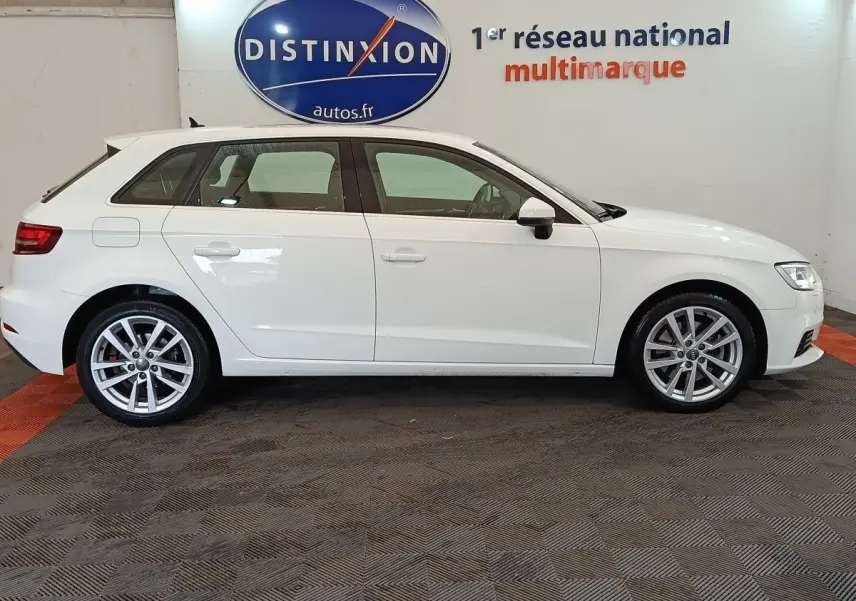 Audi A3 blanc vue de profil côté gauche, en intérieur, avec jantes alliage et logo Distinxion en arrière-plan.