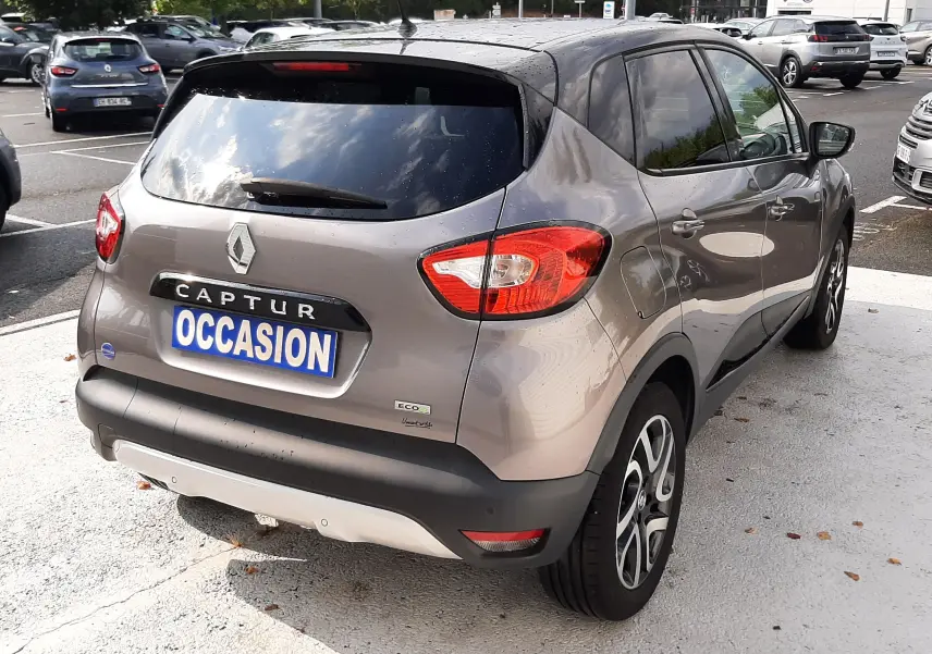 Vue 3/4 arrière droite du Renault Captur gris Cassiopée avec toit noir, en stationnement sur parking extérieur.
