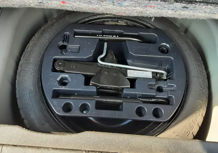 Gros plan sur la roue de secours et le kit d'outils dans le coffre du Renault Captur gris cassiopée toit noir.