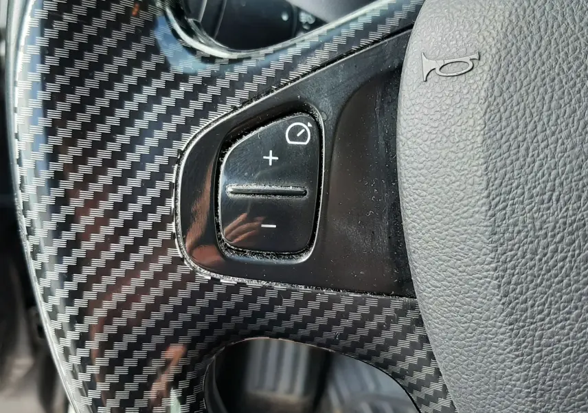 Gros plan sur le volant gris avec insert carbone du Renault Captur, montrant les commandes de régulateur de vitesse.