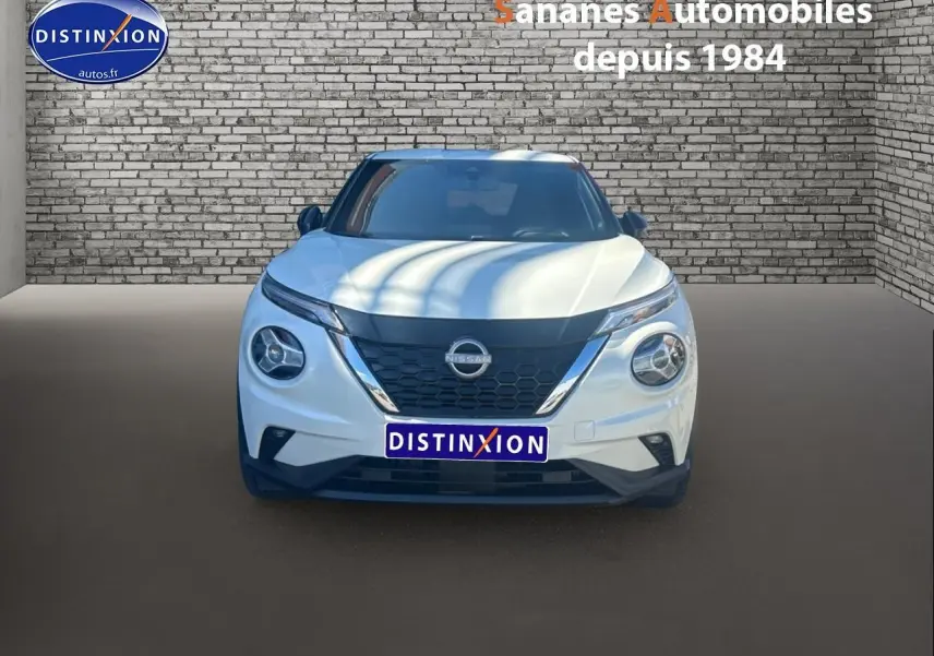 Vue frontale d'un Nissan Juke blanc 2024 avec calandre noire et phares ronds distinctifs sur fond de mur en briques.