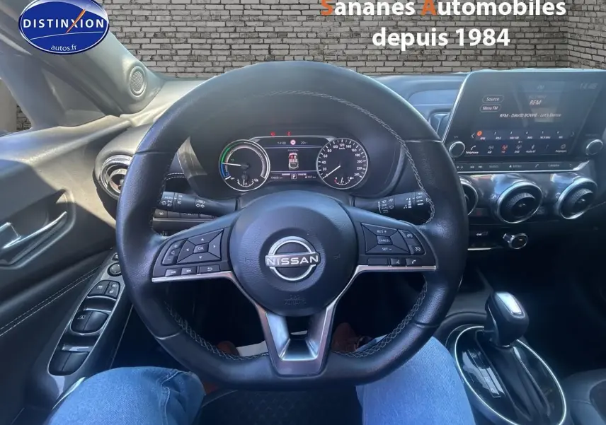 Vue intérieure centrée sur le volant et tableau de bord du Nissan Juke blanc 2024 avec écran tactile et commandes au volant.