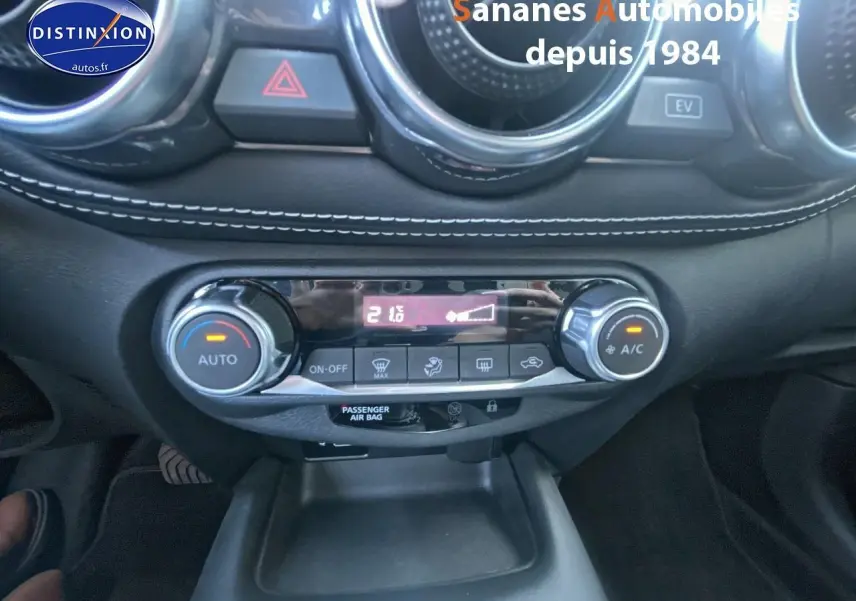 Vue rapprochée du tableau de bord du Nissan Juke blanc 2024, mettant en valeur la climatisation automatique et les commandes centrales.