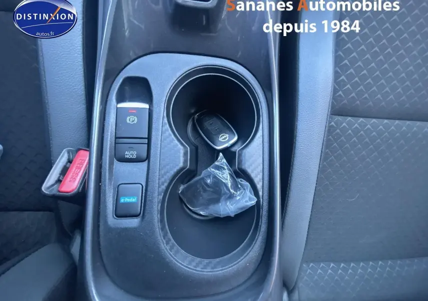 Gros plan sur la console centrale noire du Nissan Juke 2024 avec clé, bouton e-Pedal et frein à main électrique.