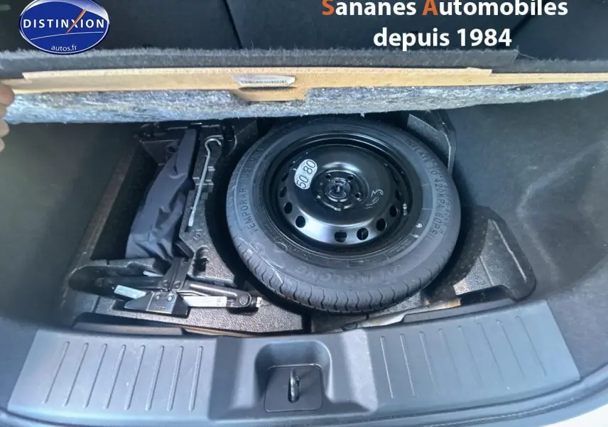 Vue plongeante sur la roue de secours noire et les outils dans le coffre du Nissan Juke blanc 2024.
