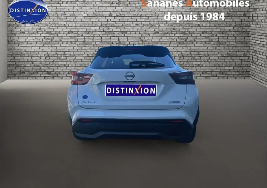 Vue arrière d'un Nissan Juke blanc 2024 hybride avec toit noir et feux arrière fumés dans un studio.