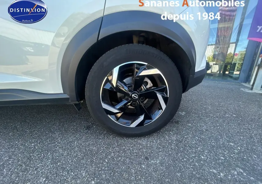 Gros plan sur la roue avant droite du Nissan Juke blanc 2024 avec jante alliage noire et chromée.