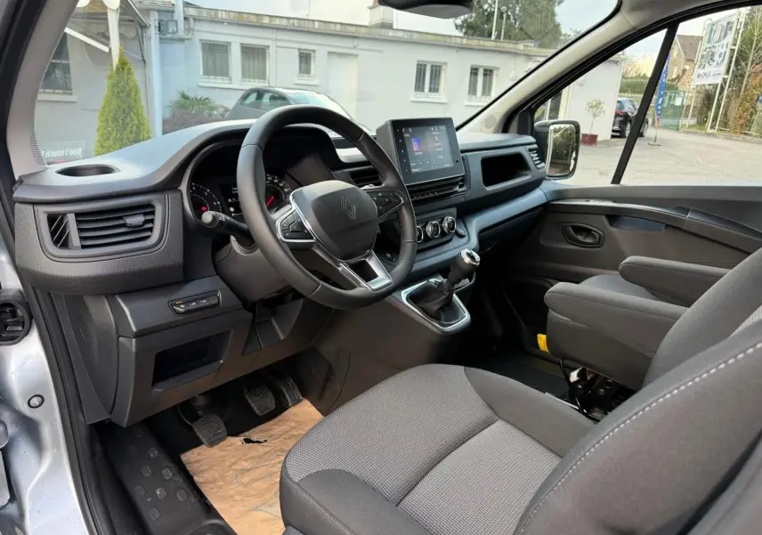 Volant noir avec logo Renault au centre, vue rapprochée de l'intérieur côté conducteur du Trafic cabine approfondie gris Highland 2025.