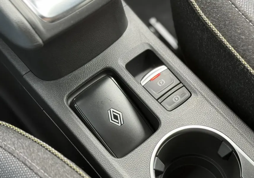 Gros plan sur la console centrale noire du Renault Captur blanc nacré, avec frein à main électrique et porte-clés Renault.