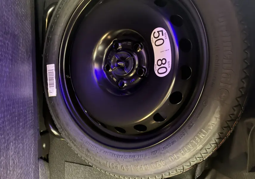Roue de secours noire avec étiquette de vitesse 50 mph/80 km/h, logée dans le coffre d'un Renault Captur 2025 hybride.