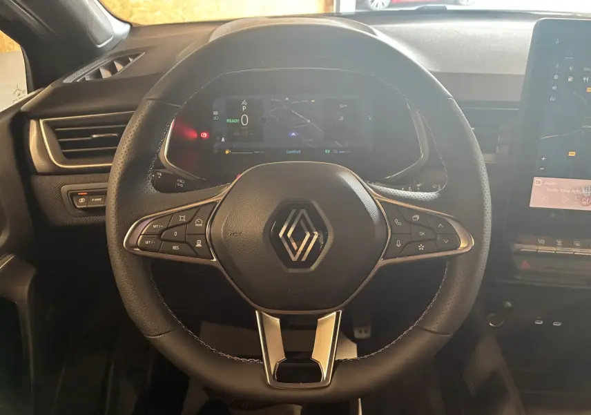 Volant en cuir noir avec logo Renault au centre, tableau de bord digital et écran tactile à droite dans un Renault Captur hybride 2025.