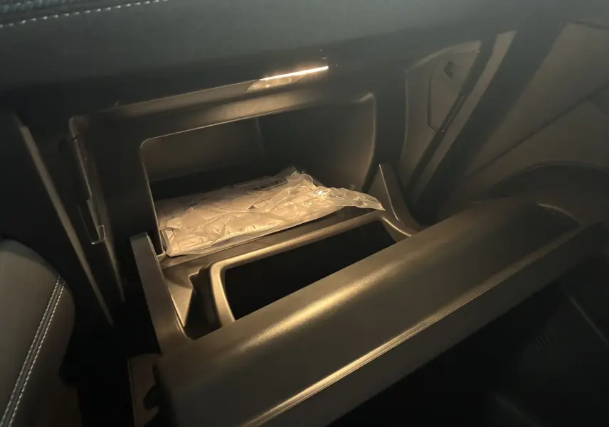 Gros plan sur la boîte à gants ouverte du Renault Captur E-Tech 2025, intérieur noir avec éclairage doux.