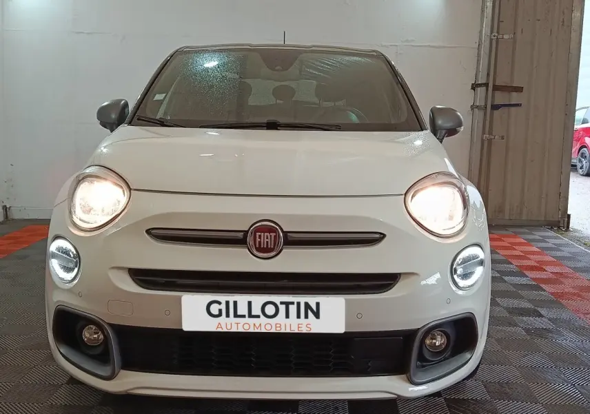 Vue avant d'une FIAT 500X blanche avec phares allumés et feux diurnes LED en intérieur.