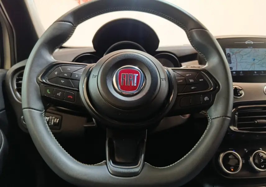 Vue rapprochée du volant noir de la Fiat 500X 2021 avec commandes intégrées et écran tactile de navigation visible.