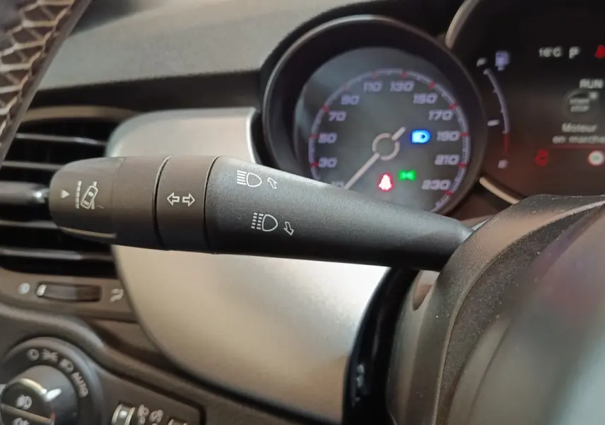 Gros plan sur la manette de clignotants noire du tableau de bord du Fiat 500X noir, avec compteur de vitesse en arrière-plan.