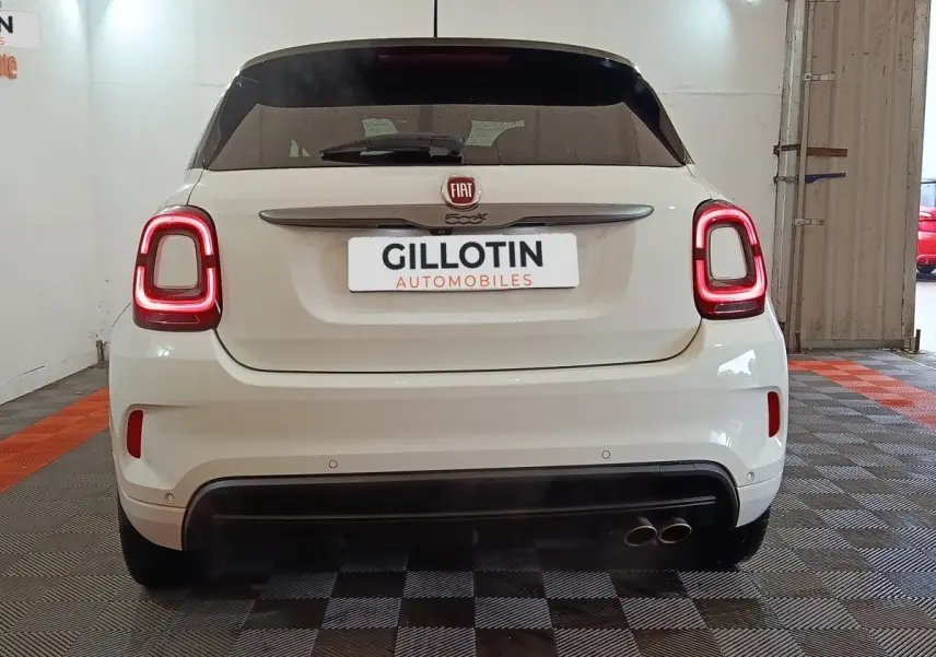 Vue arrière d'une FIAT 500X blanche avec feux arrière LED allumés et double sortie d'échappement à droite.