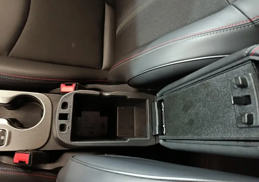 Vue rapprochée de la console centrale ouverte avec accoudoirs noirs et surpiqûres rouges dans un Fiat 500X noir.