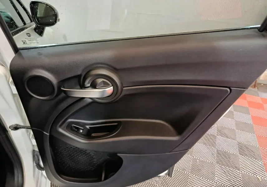 Vue intérieure de la porte arrière gauche noire du Fiat 500X, avec poignée argentée et commande de fenêtre.