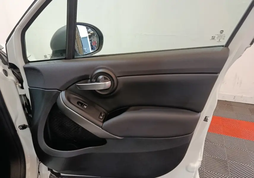 Vue intérieure de la porte avant gauche noire d'une FIAT 500X 2021 avec poignée argentée et commandes de vitres.